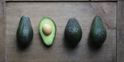 A row of avocados but one is cut in half with the pit visable.