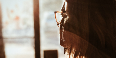 Backlit image of woman in glasses contemplating through a window.